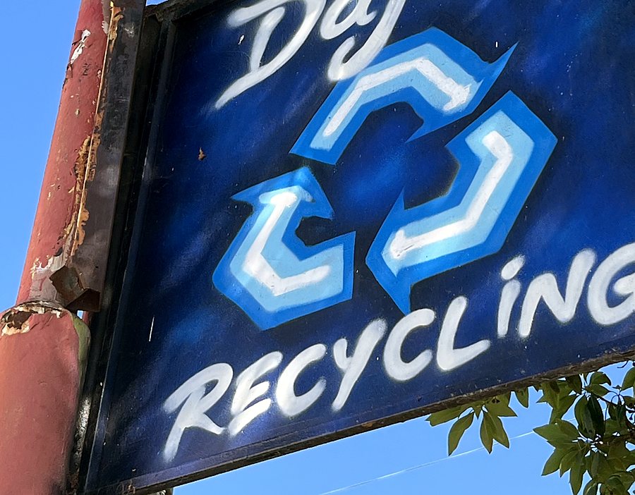 The blue hand-painted DÀJÉS Recycling sign with the recycling arrows