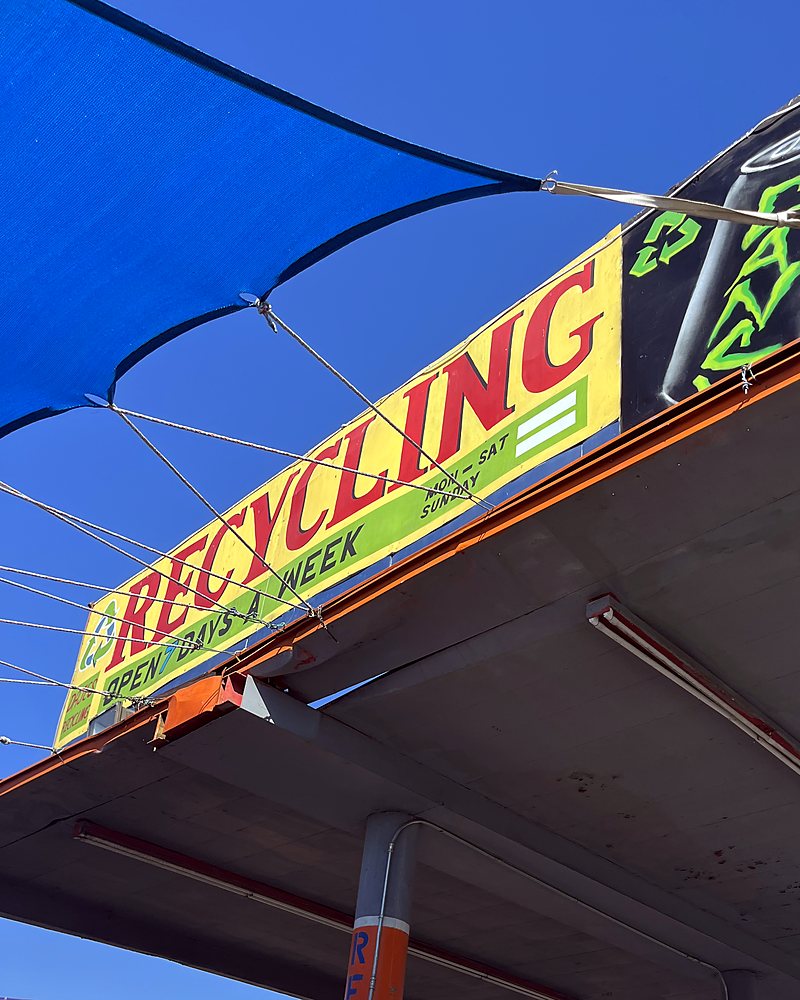 The yellow and red RECYCLING sign on the roof of the DÀJÉS yard, seen from below against a blue sky