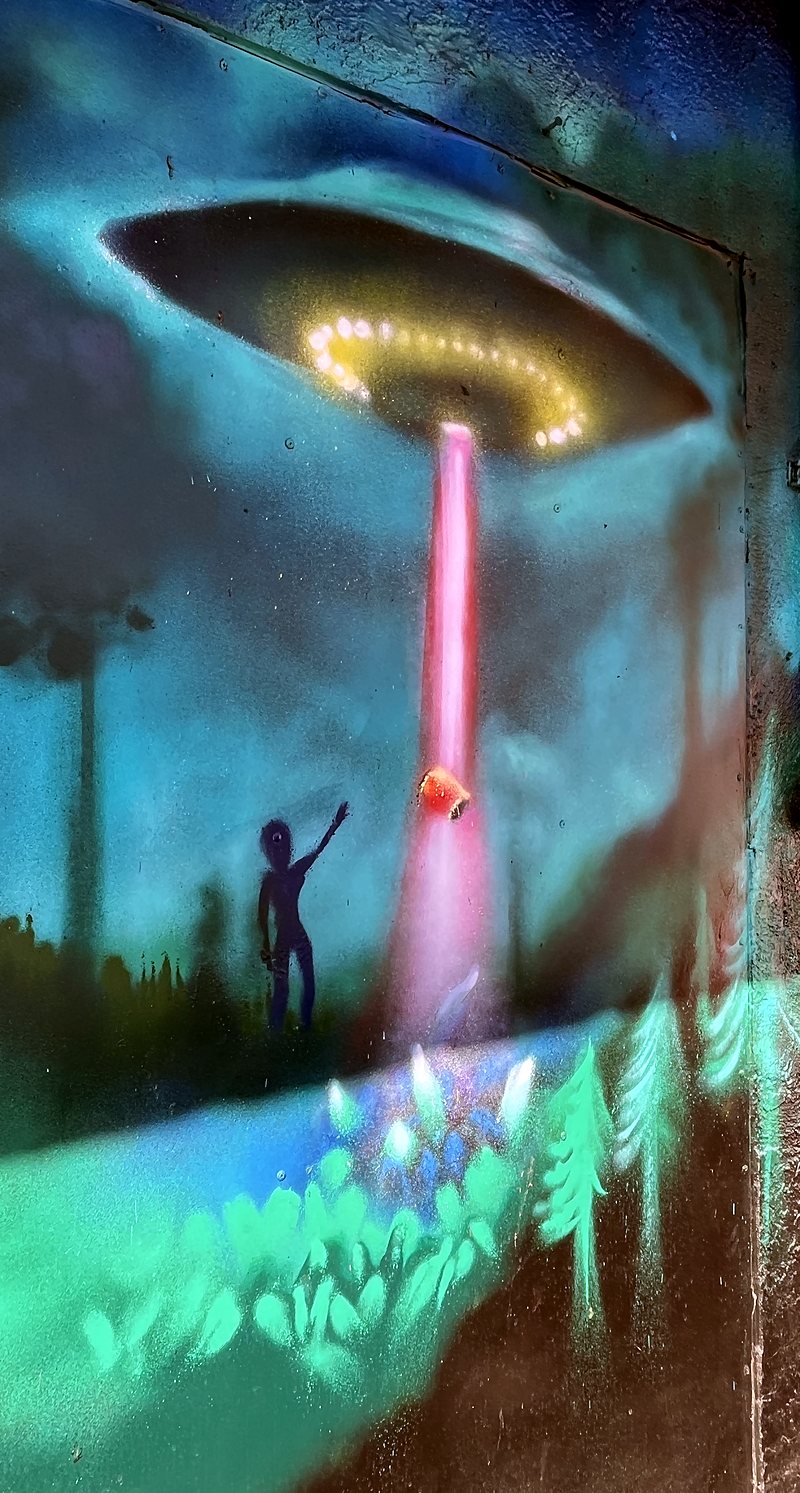 A painted mural on the yard wall: a flying saucer beaming up a figure at night