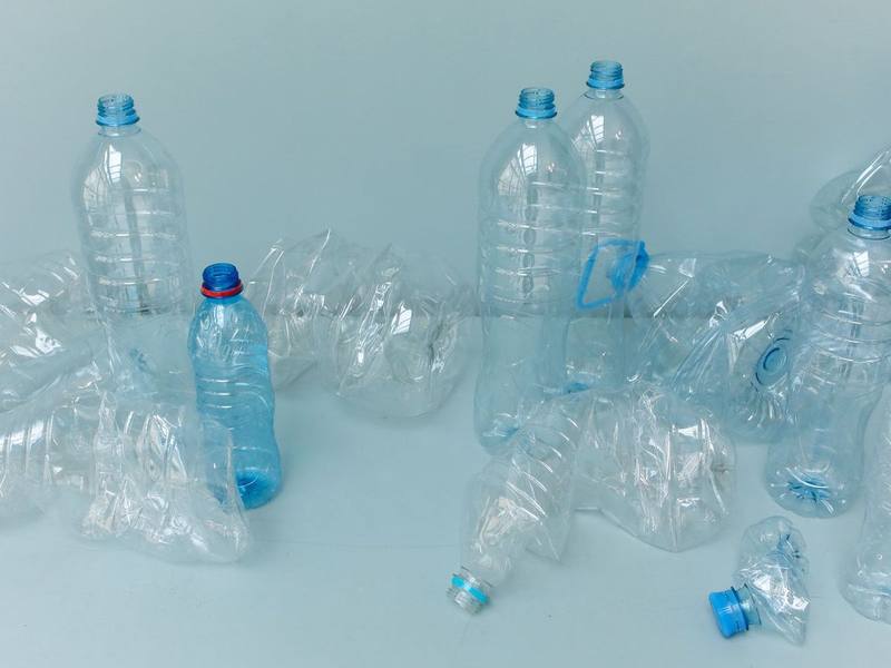 Clear plastic water bottles, some standing and some crushed, on a light blue surface